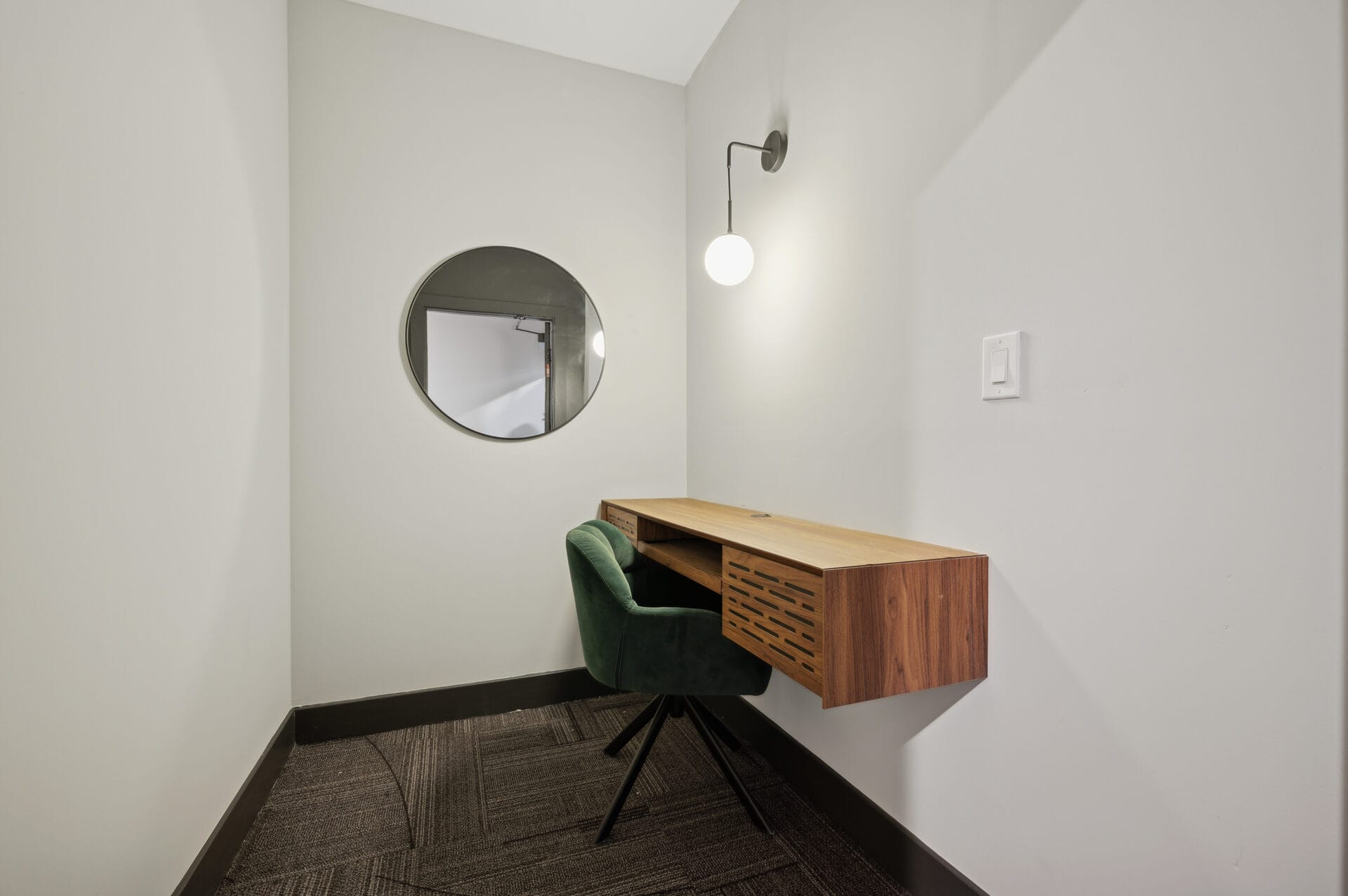 Private co-working nook at The Lane with walnut floating desk, green velvet chair, and globe sconce